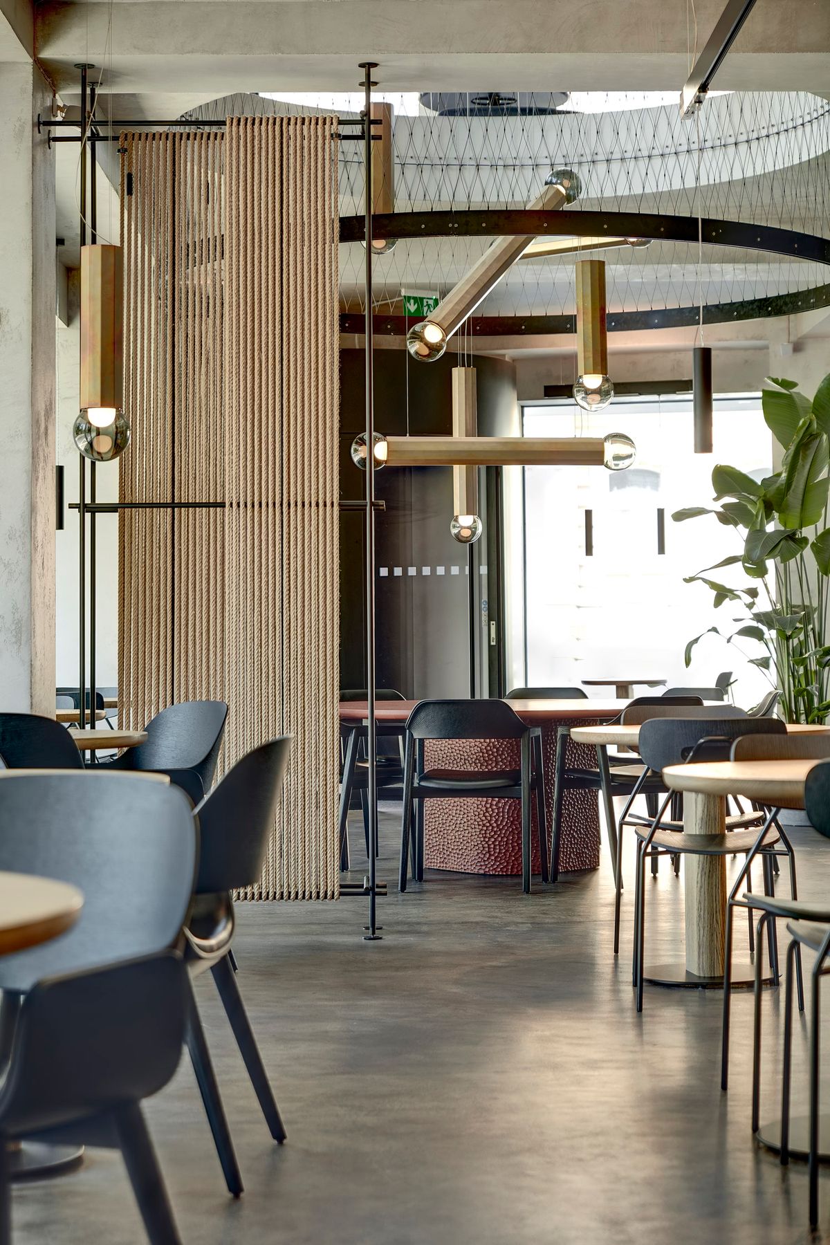 Modern café with minimalist black chairs, round wooden tables, Brokis Prisma lighting, and airy industrial-luxe accents.