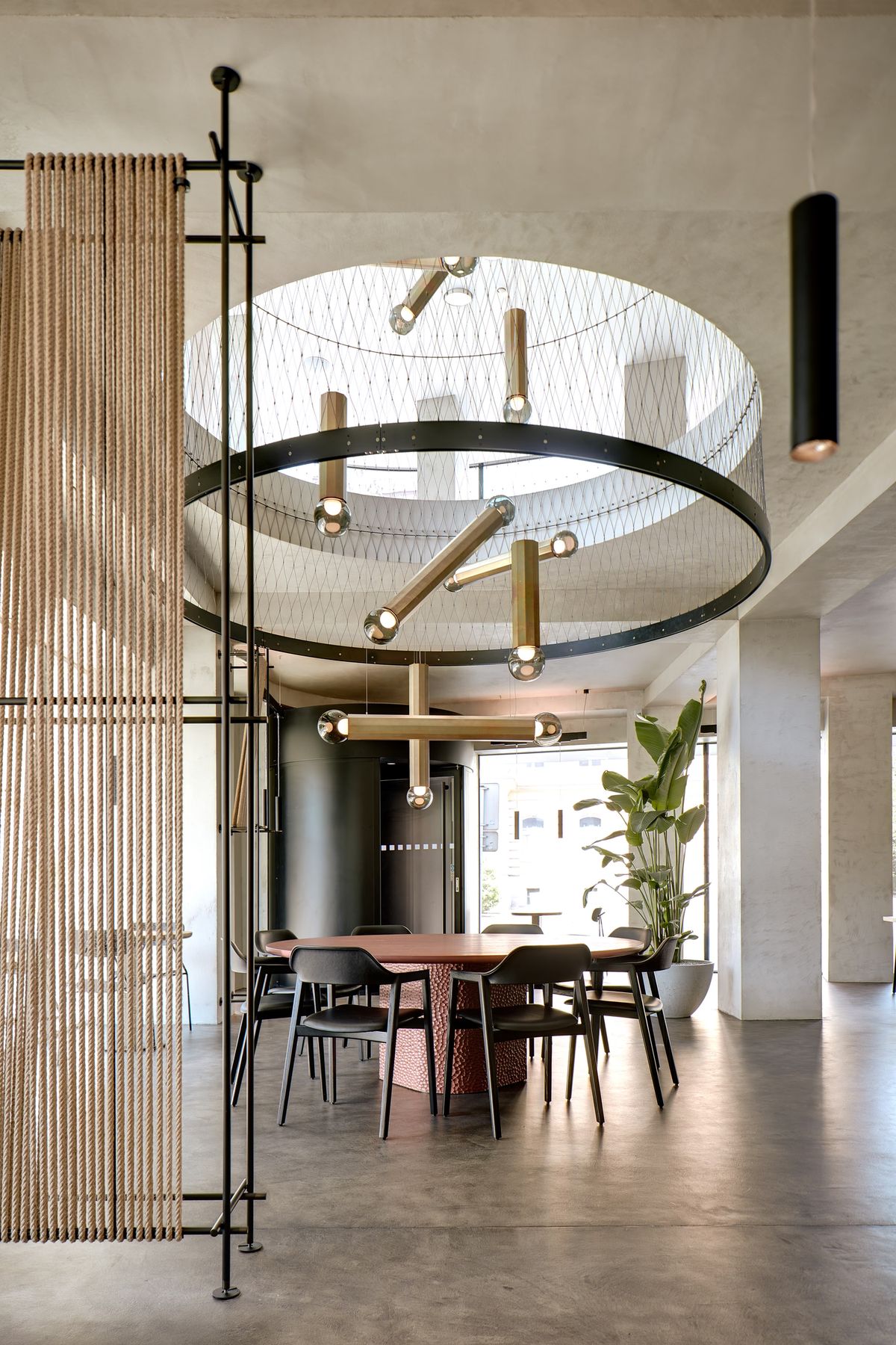 Modern dining room with a round wooden table, black chairs, sculptural gold chandelier, skylight, and Brokis Prisma lights.