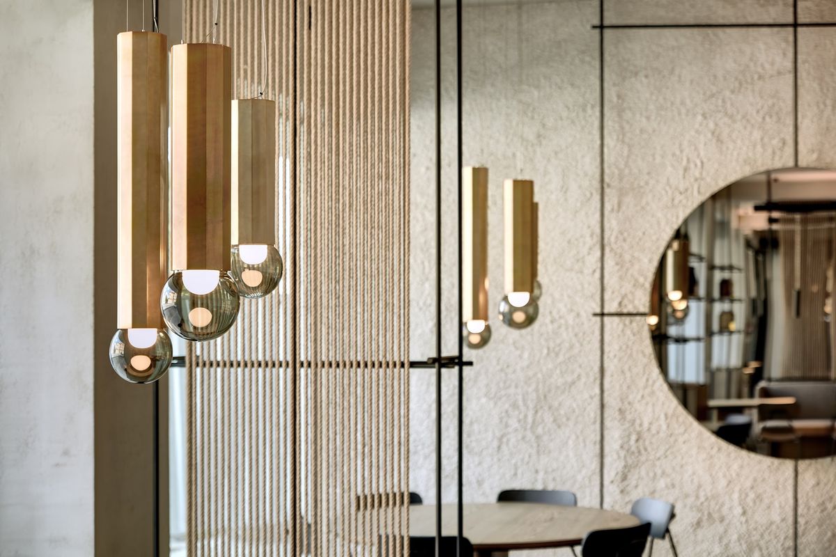 Brokis Prisma Single pendants with metallic accents hang near a rope divider, mirrored in a luxe minimalist interior.