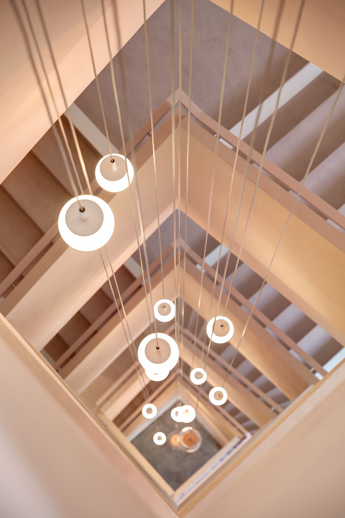 A soaring spiral staircase with beige walls and railings, Brokis Sfera pendants cascade in luminous tiers.