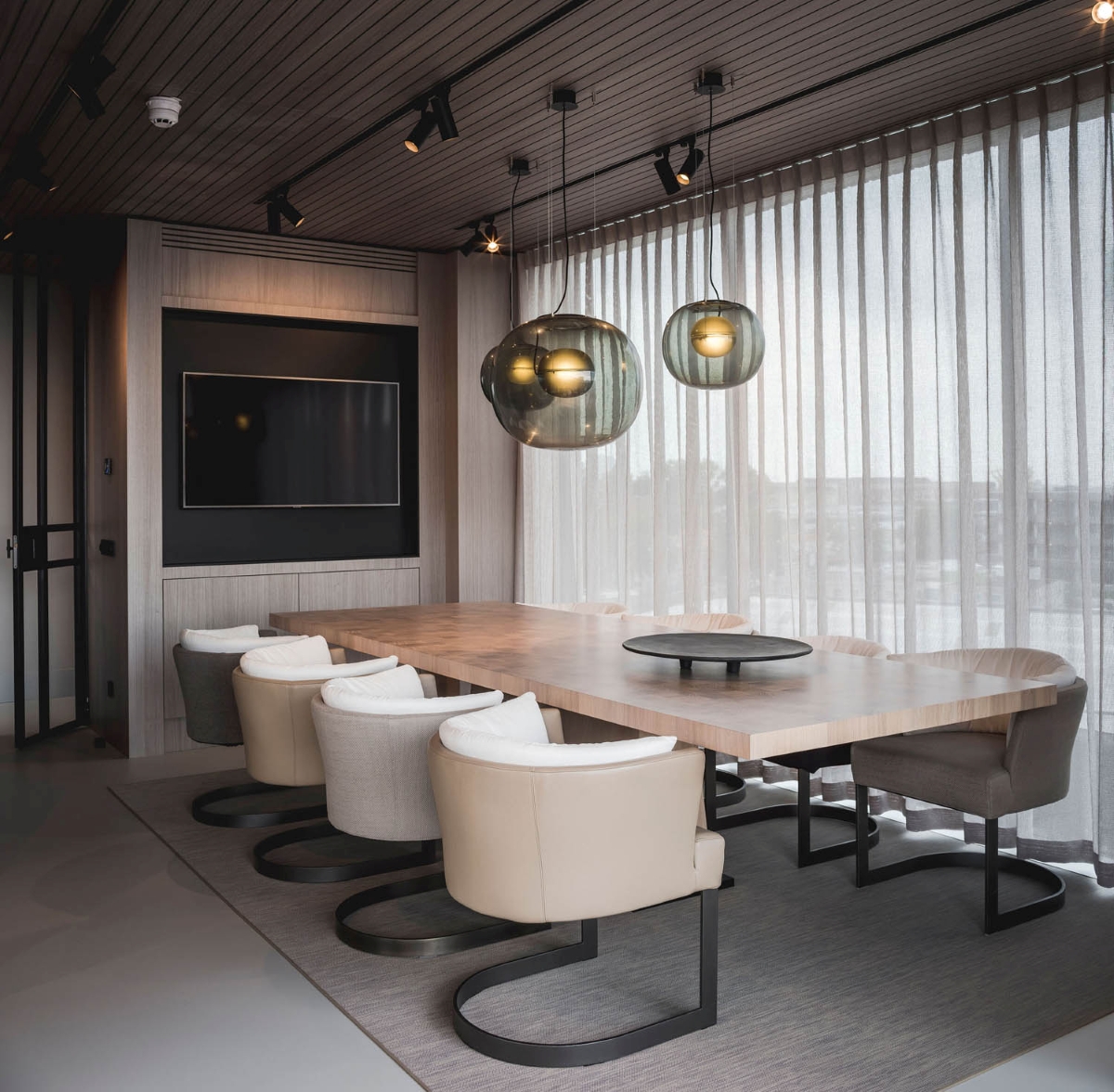 Elegant conference room with a long wooden table, Brokis Big One pendants, sheer curtains, and luxe minimalist furnishings.