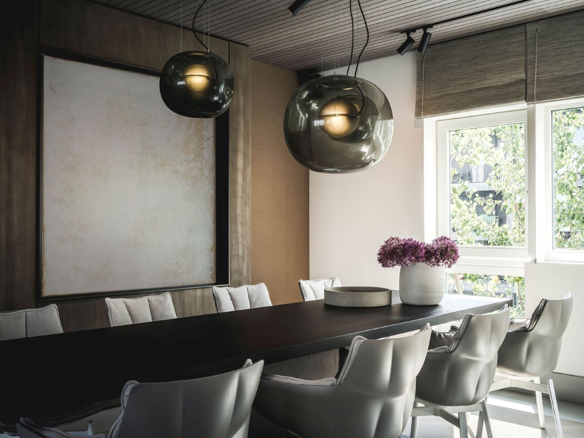 Elegant dining room Big One pendants, a dark table, white chairs, purple flowers, and a sunlit art wall.