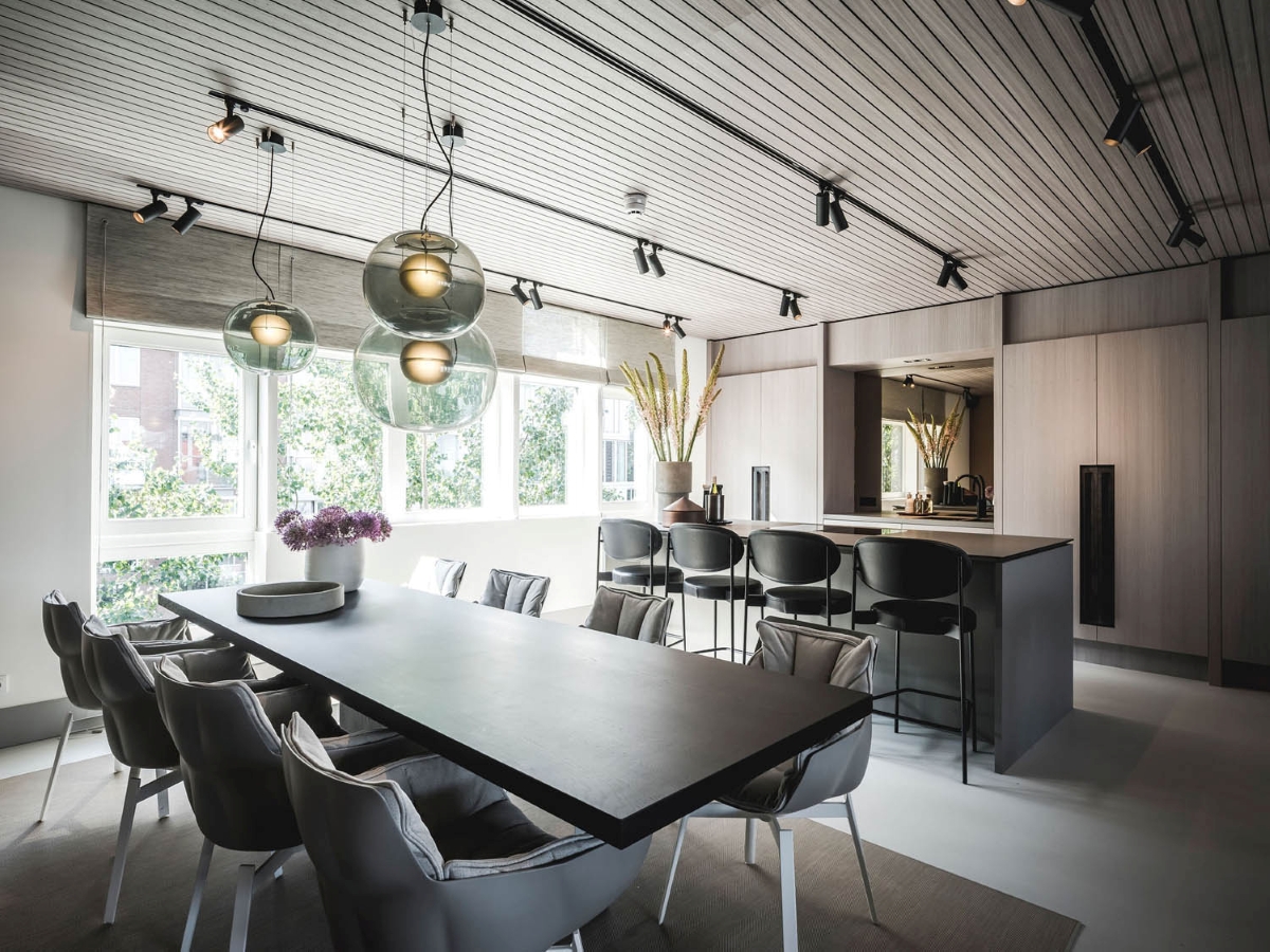 Sleek office space with a long black table, plush grey chairs, and island. Brokis Big One pendants glow above.