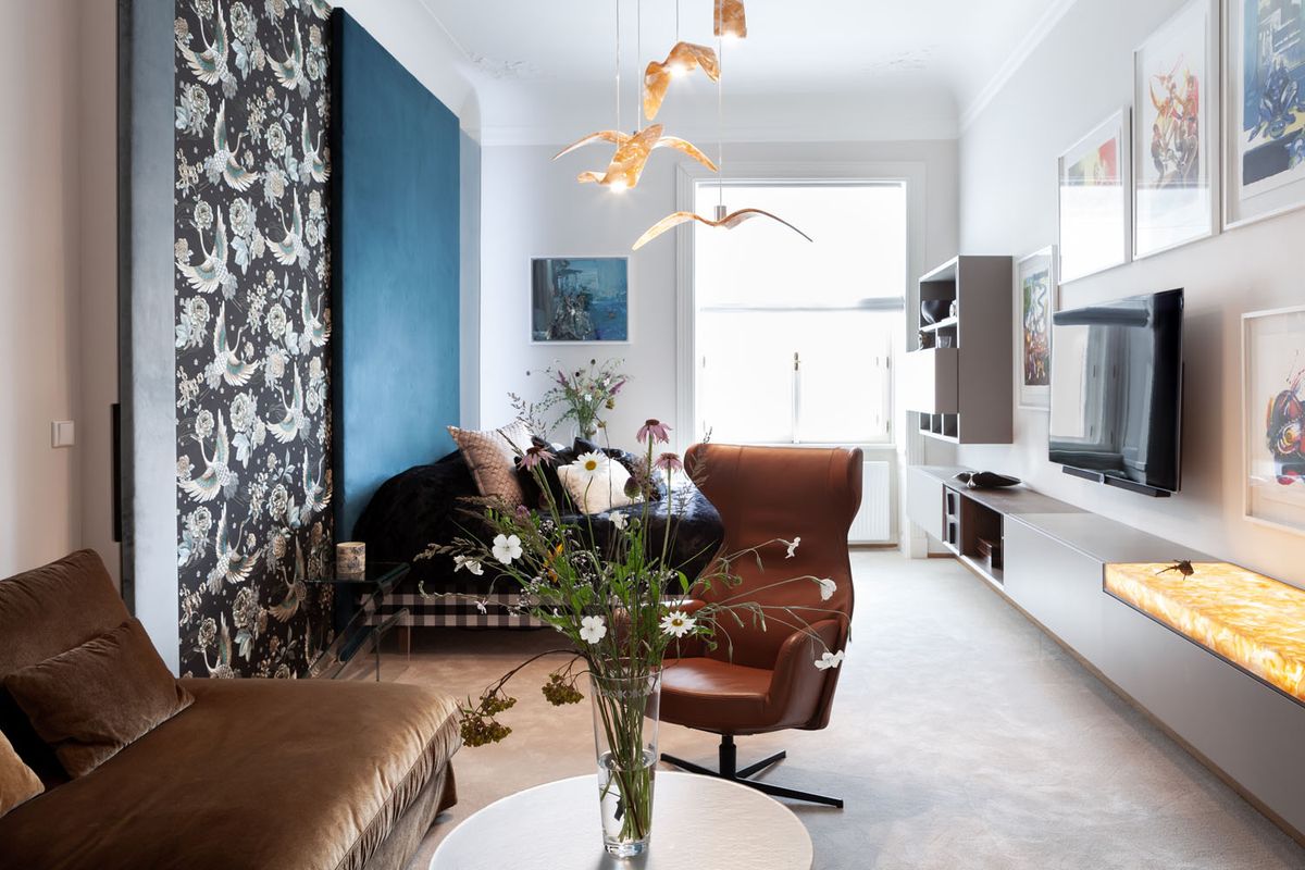 A modern living room with a brown sofa, sleek armchair, white table, Brokis Night Birds pendants, and curated art.