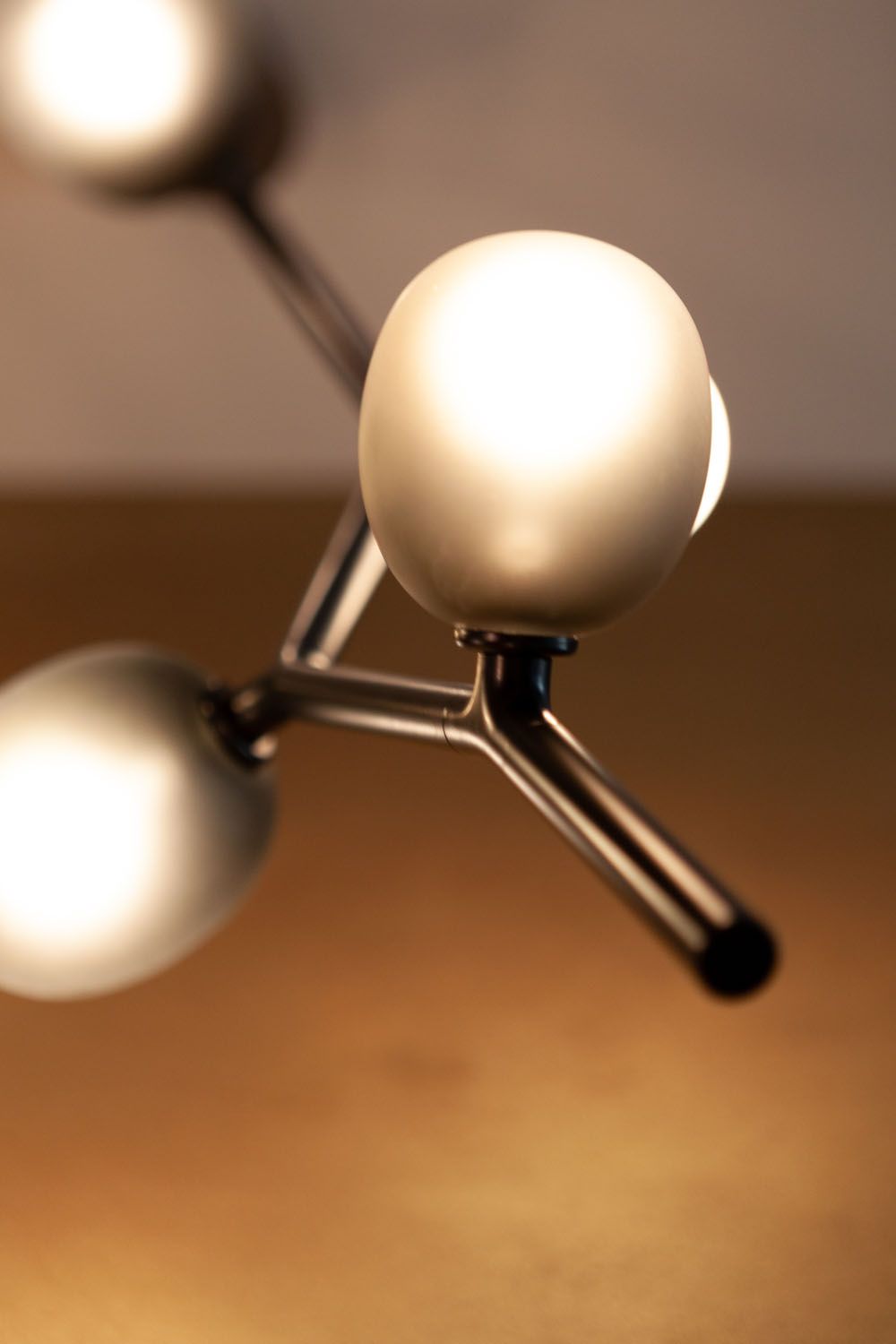 Close-up of Brokis Ivy pendant with hand-blown frosted glass globes and metallic arms, glowing against a blurred backdrop.