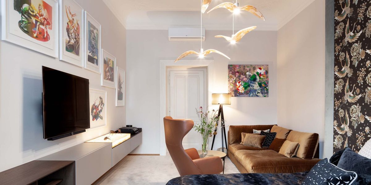 Modern living room with brown sofa, blue armchair, brown lounge chair, art on pale walls, and Brokis Night Birds pendants.