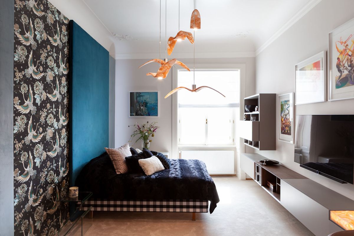 Bedroom with a black bed, feature wall, teal backdrop, Brokis Night Birds pendants, art, flowers, and natural light.