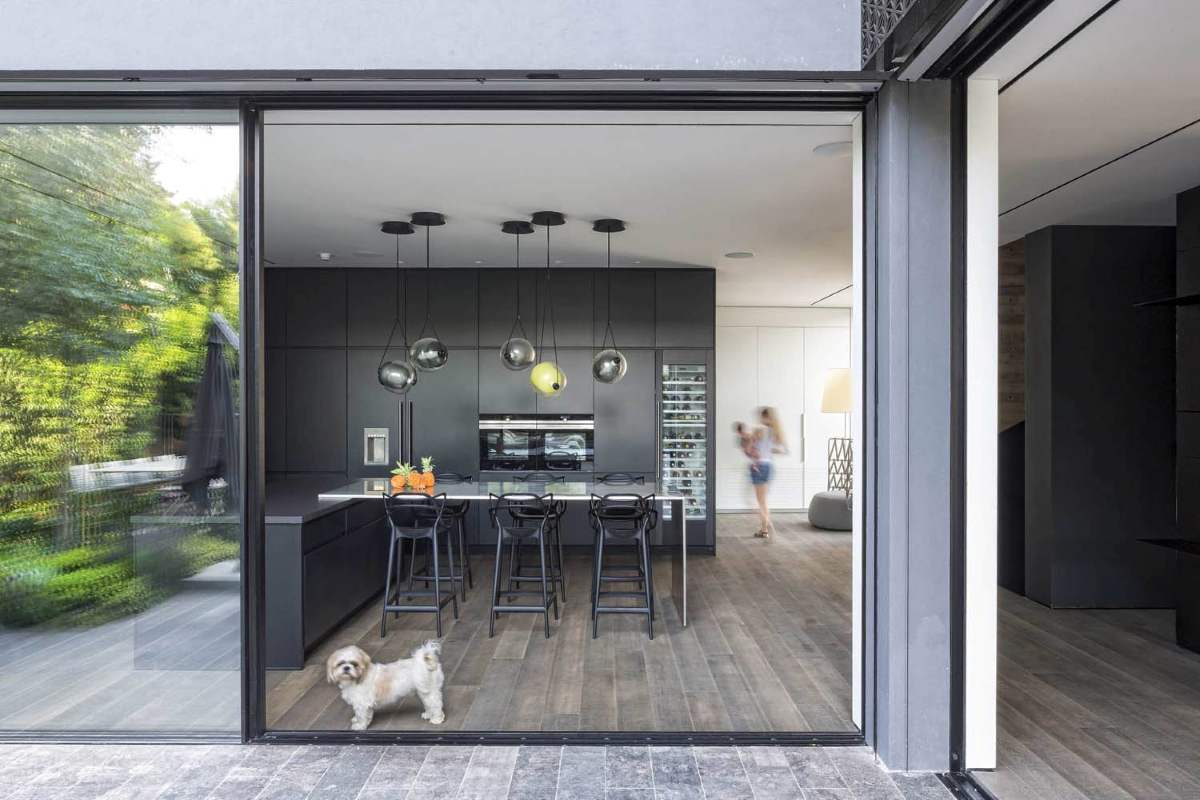 Sleek kitchen with dark cabinetry, a central island, Brokis Capsula Single Pendants, black bar stools, and garden views.