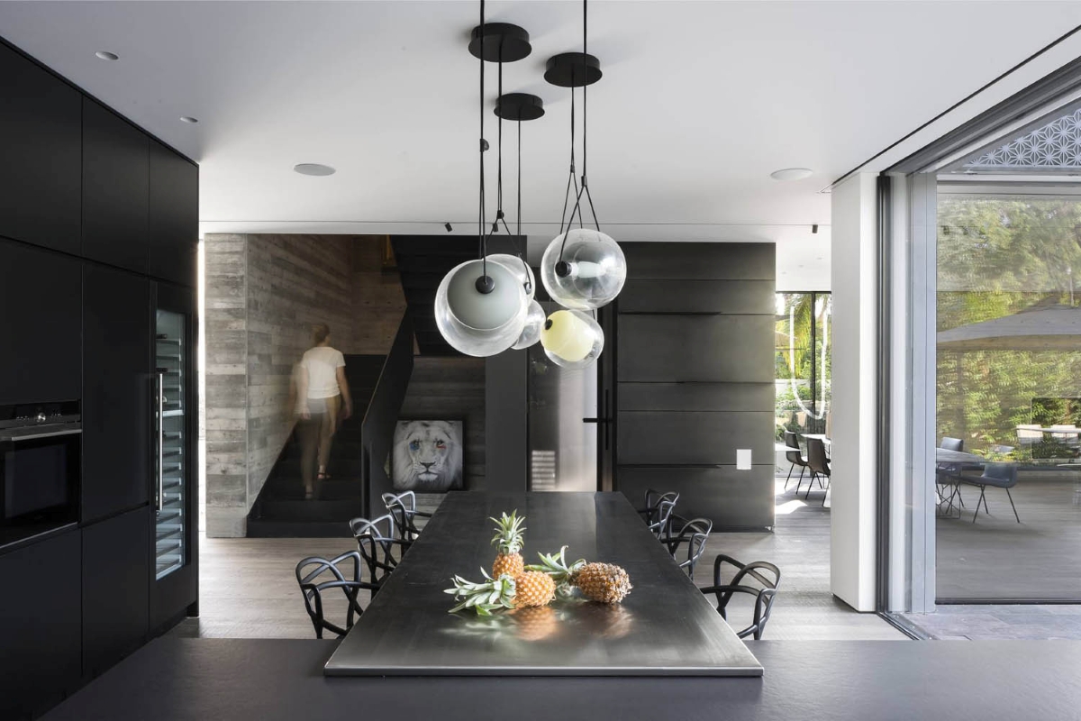 A modern kitchen with a black table topped with pineapples, Brokis Capsula Single Pendants, and views to greenery.