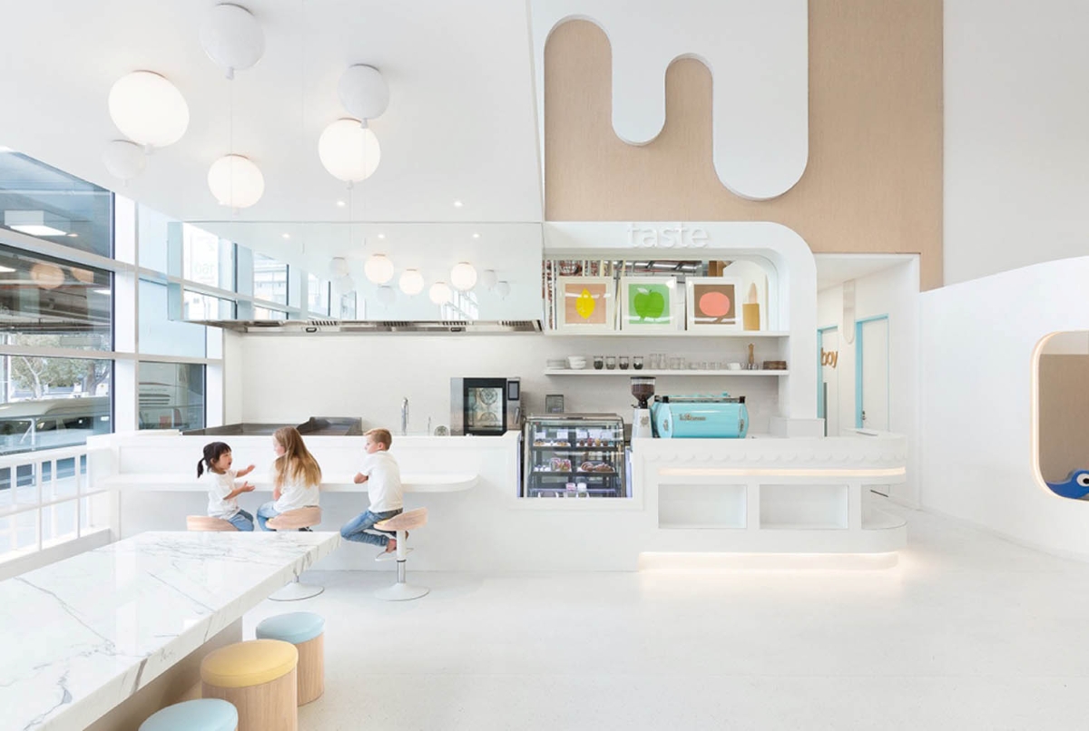 A luminous café with white walls, pastel tones, Brokis Memory ceiling lights, marble counter, and sleek blue coffee machine.