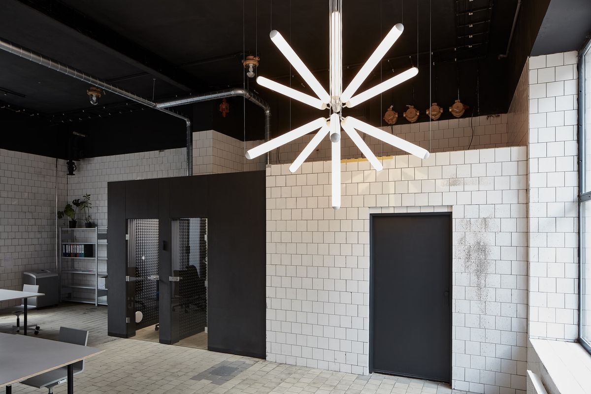 A modern office with white tiled walls, a dark ceiling, and a Brokis Puro Sparkle Chandelier radiates luxury allure.