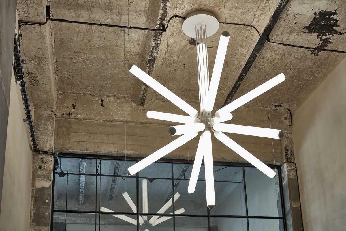 Brokis Puro Sparkle 1000 Chandelier with glowing rods radiates in an airy industrial loft with exposed wiring.