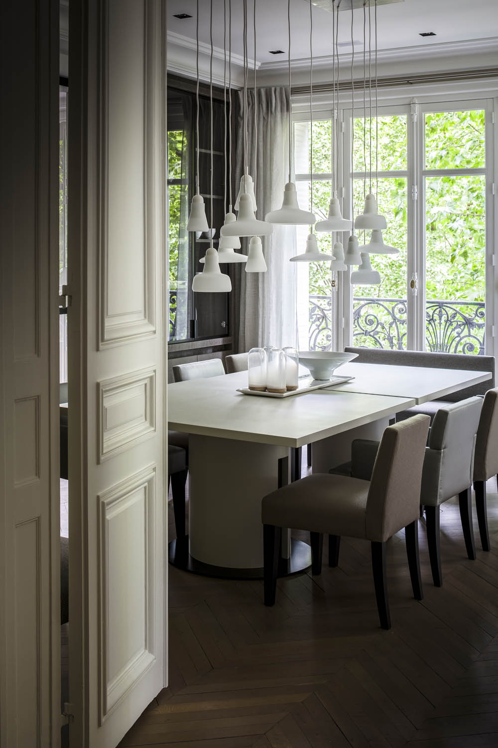 A modern dining room with a light wood table, beige chairs, white Brokis Shadows pendants, and herringbone wood floors.
