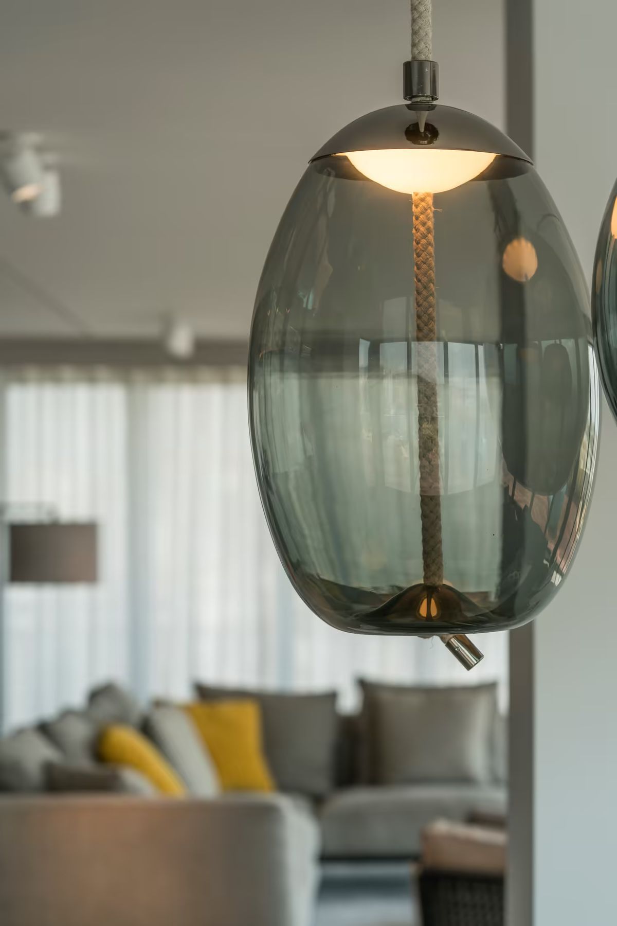 Close-up of Brokis Knot Uovo Pendant with grey glass shade, glowing above a luxurious, softly blurred modern interior.
