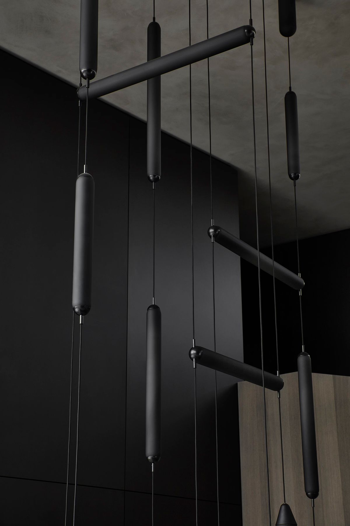 Brokis Puro pendants with black cylindrical bars, suspended by fine cords against a luxe, minimalist wood and black setting.