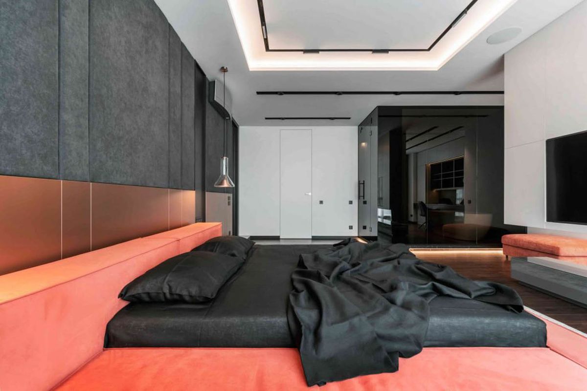 A luxe bedroom with a coral bed frame, black bedding, Brokis Whistle Small Pendants, mirror, TV, and dark panelled walls.