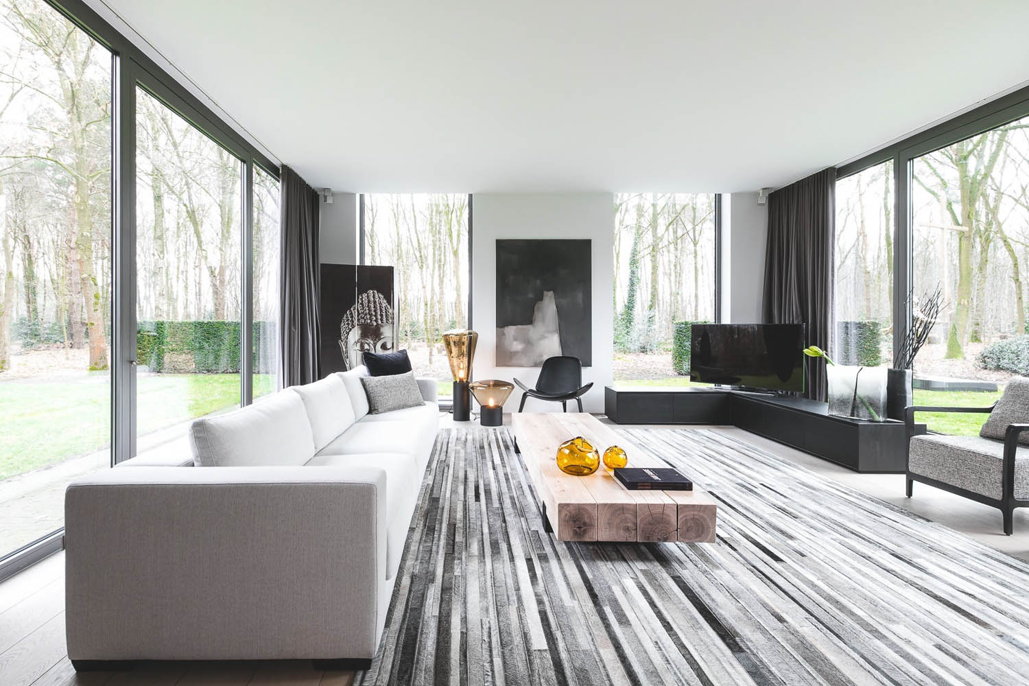 Living room with floor-to-ceiling windows, striped carpet, sofa, coffee table, Brokis Muffins floor lamps and forest views.