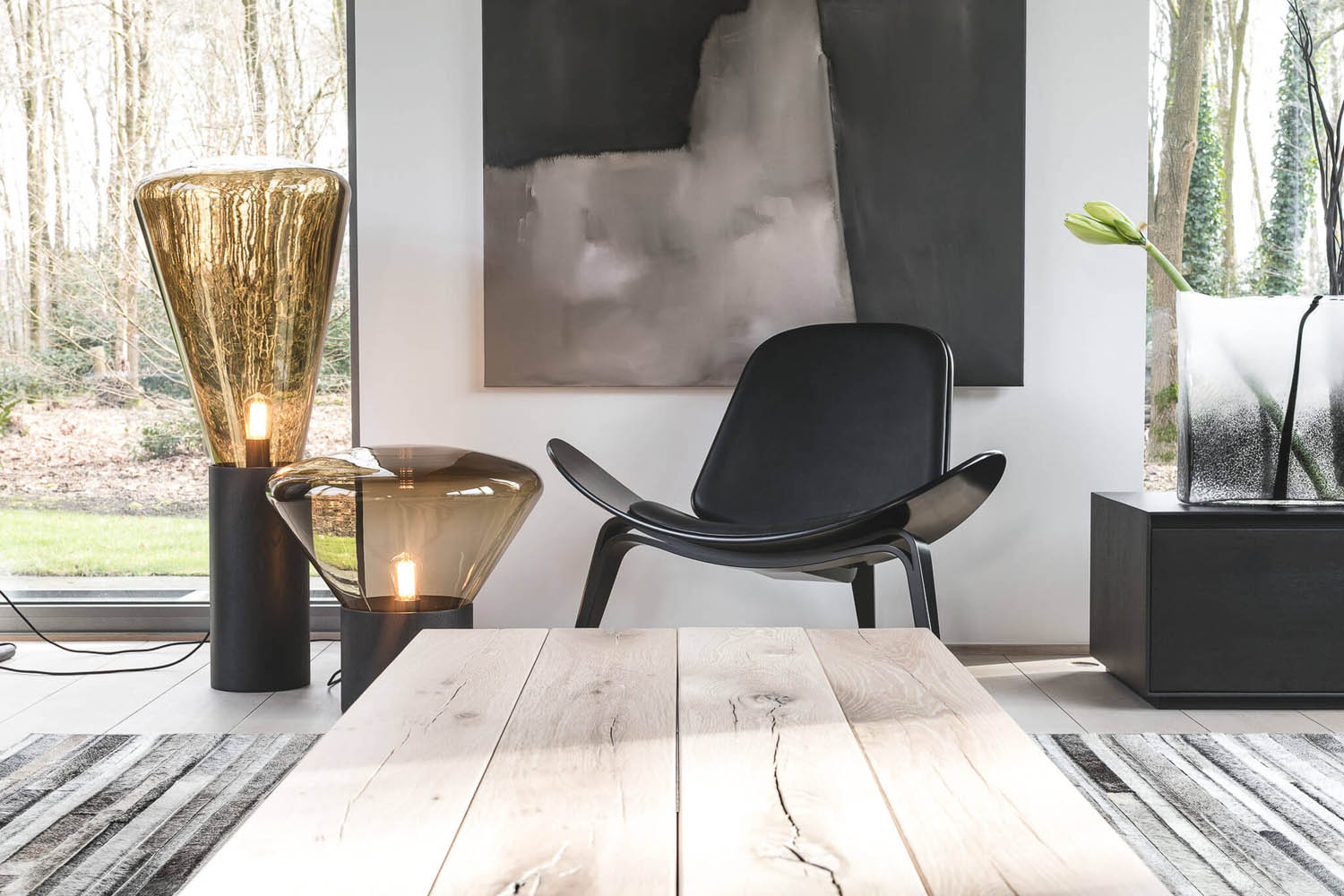 A modern living room with a black lounge chair, Brokis Muffins floor lamps, bold abstract art, and fresh tulips.