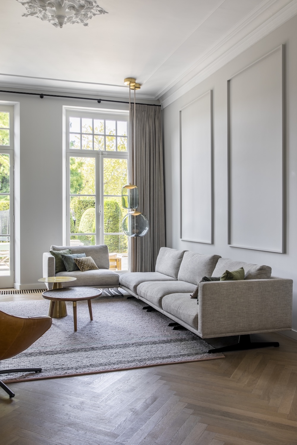 Elegant living room with vast windows, minimal decor, plush grey sectional, wooden coffee table, and Brokis Knot pendants.
