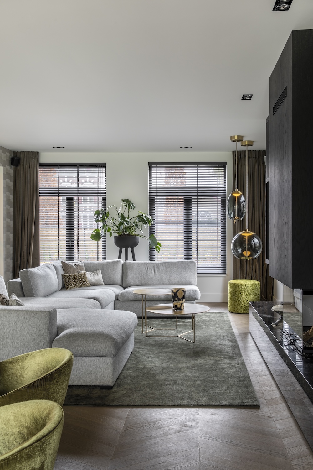 Sophisticated living room with a light-grey sectional, green velvet chairs, Brokis Knot pendants, and sleek black fireplace.