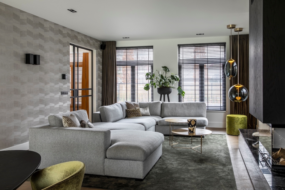 A modern living room with a light grey sectional, geometric wallpaper, gold coffee table, and Brokis Knot pendants.