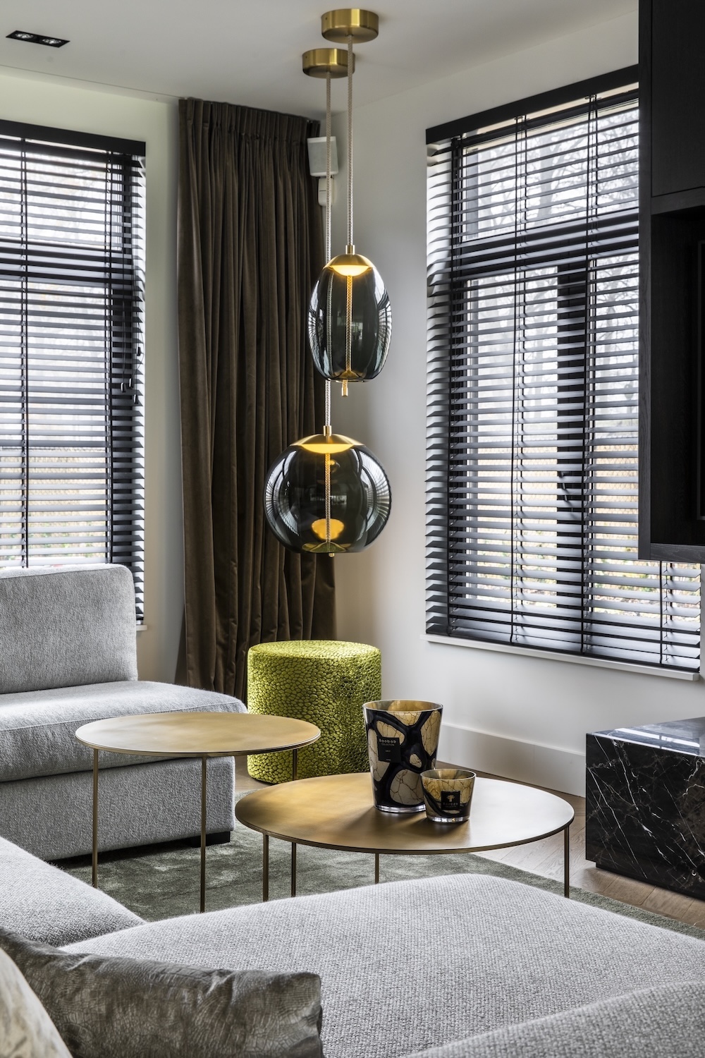 Modern living room with grey sofas, nested wooden tables, green stool, and Brokis Knot pendants.