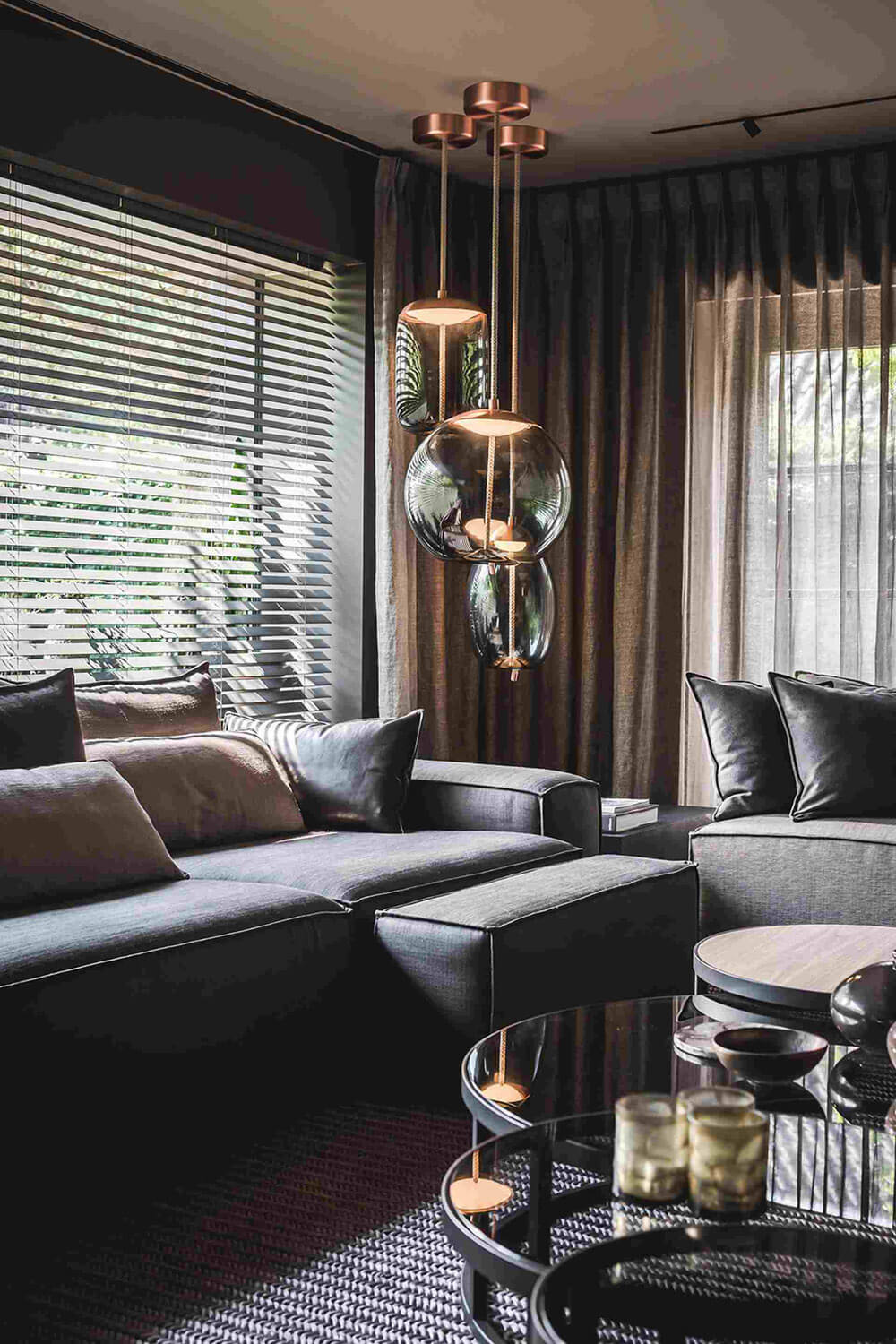 A modern living room with a dark grey sectional, Brokis Knot pendants, and elegant neutral accents.