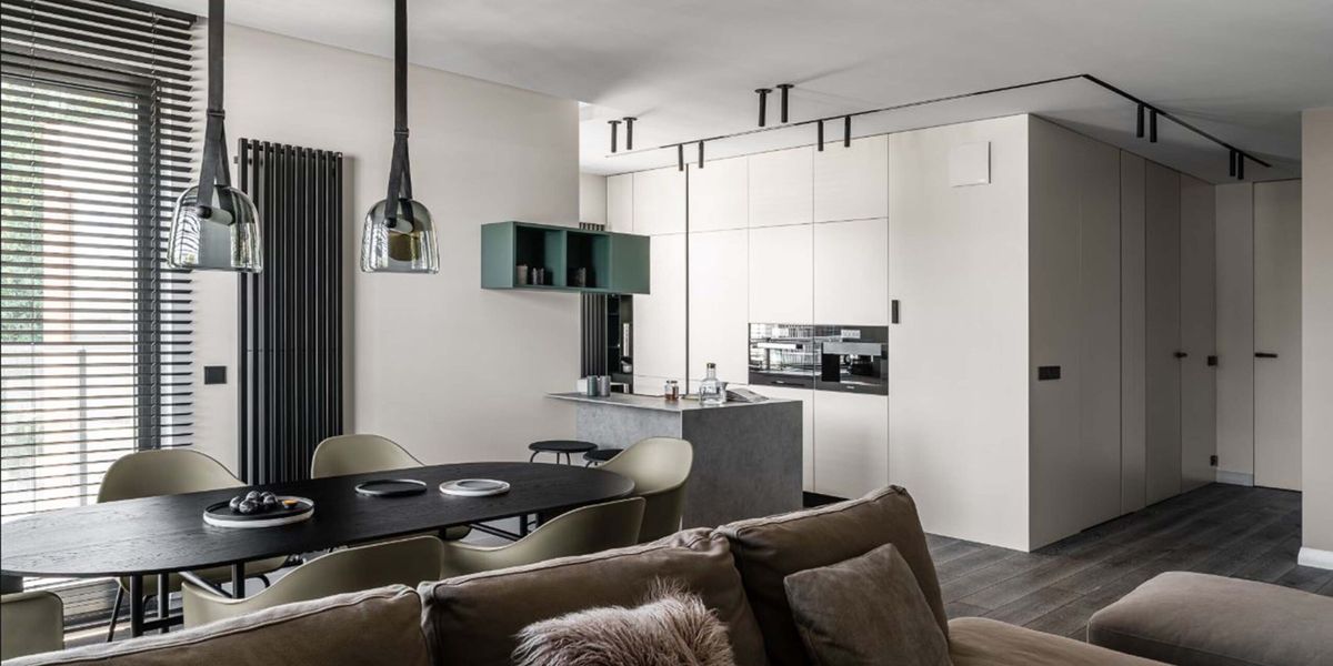 Sleek open kitchen and dining area with Brokis Mona Medium Pendants, dark wood table, beige chairs, and luxe white cabinetry.