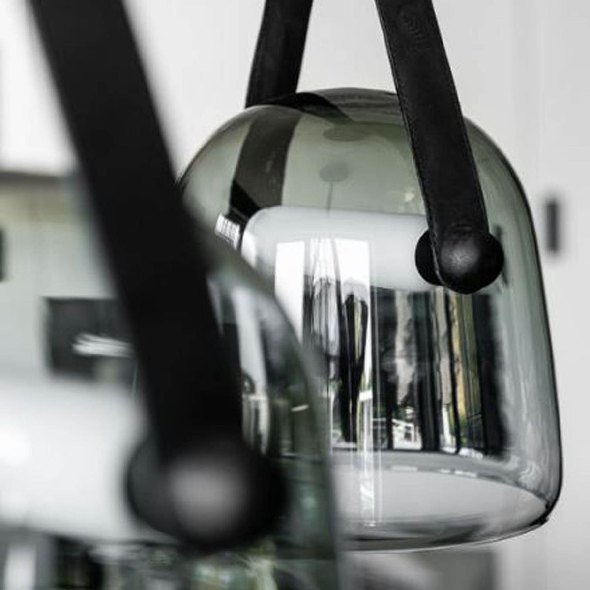 Close-up of Brokis Mona pendants in glossy smoke grey glass, their handblown shades reflecting luxurious interior details.