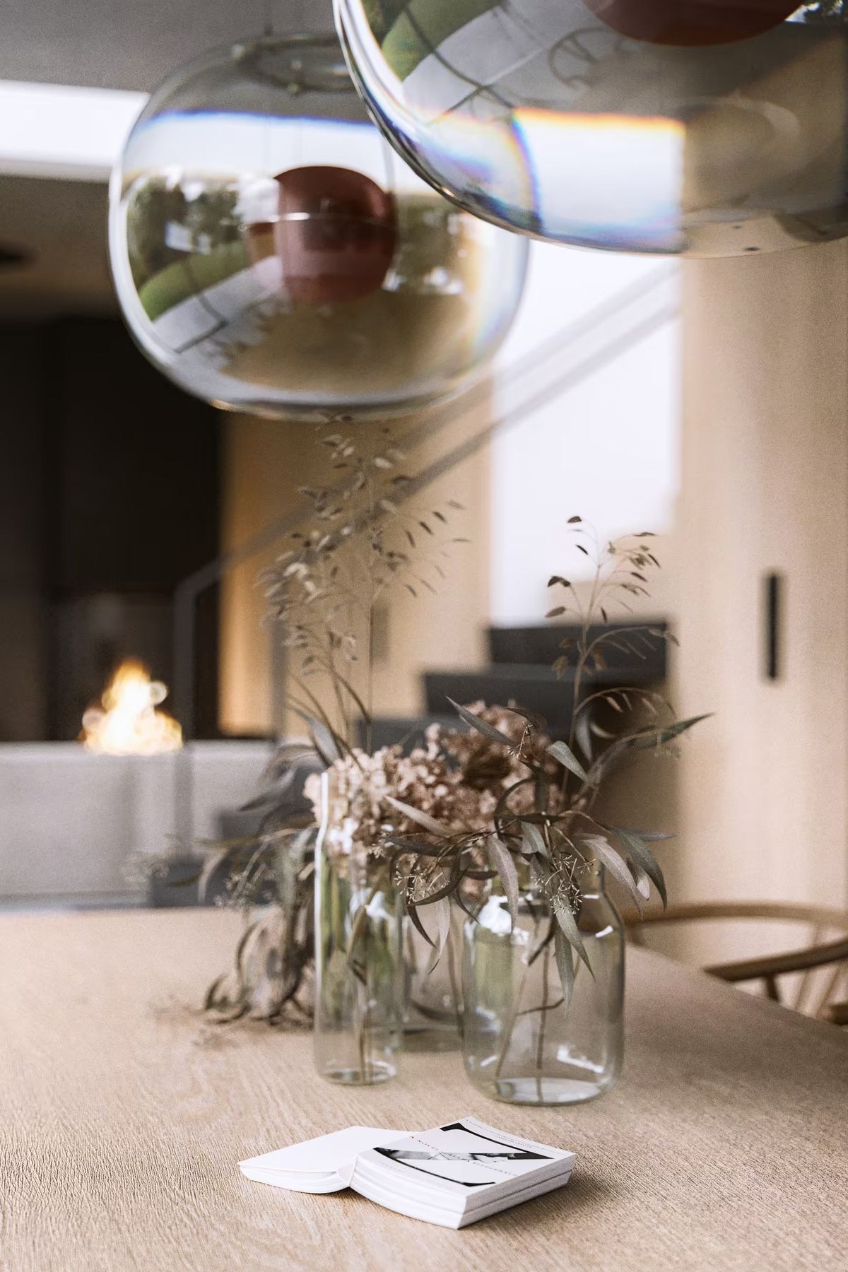 A refined table with glass vases of dried flowers, open book, and Brokis Big One Large pendants in a modern space.