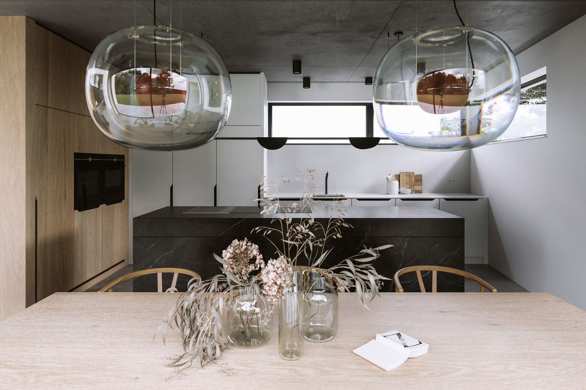 A kitchen with light wood and black finishes, a wooden table with dried flowers, Brokis Big One Large pendants overhead.