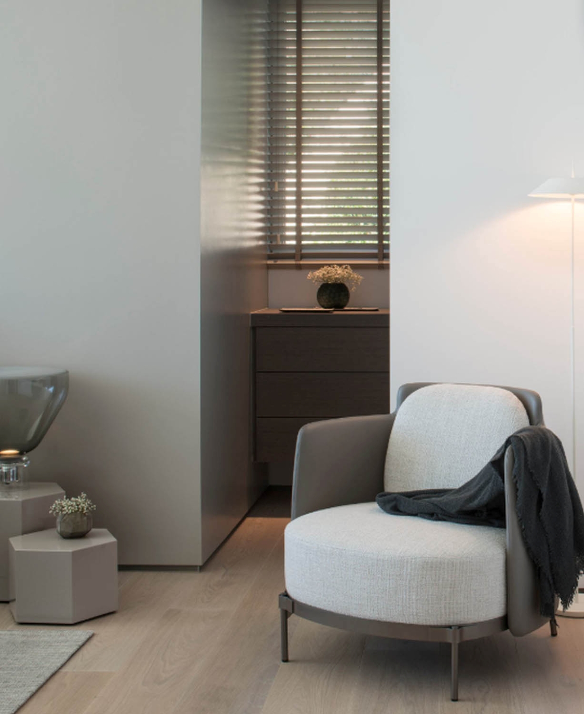 A serene, modern living room with a Brokis Lightline M, luxe grey armchair, wooden floors, and fresh flowers.