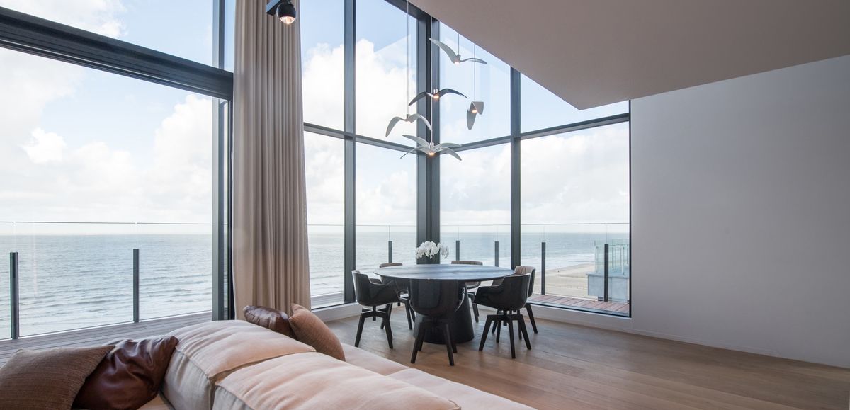 Airy living and dining area with floor-to-ceiling sea views, Brokis Night Birds pendants above round table, beige sofa.