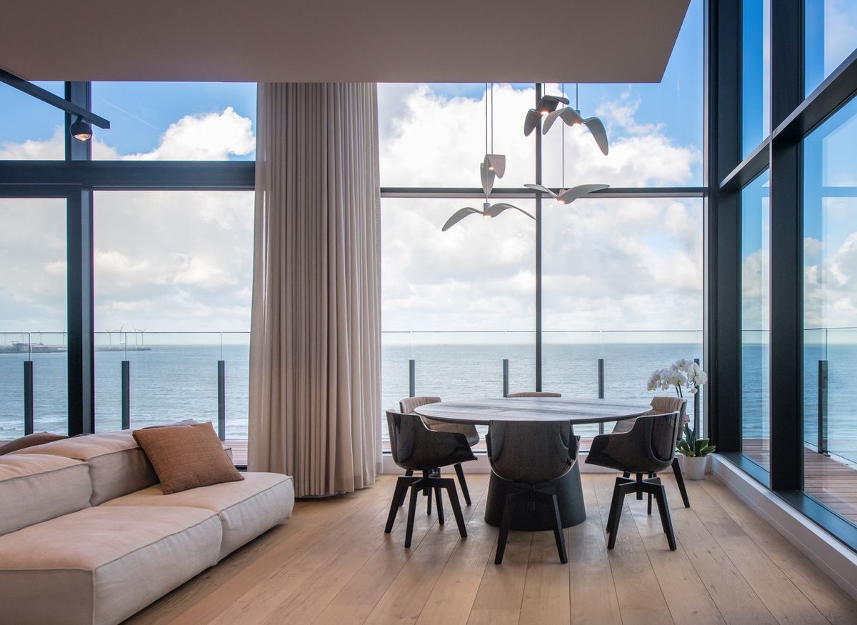 Expansive living room with sea views, Brokis Night Birds pendants, plush beige sofa, airy curtains, orchid centrepiece.