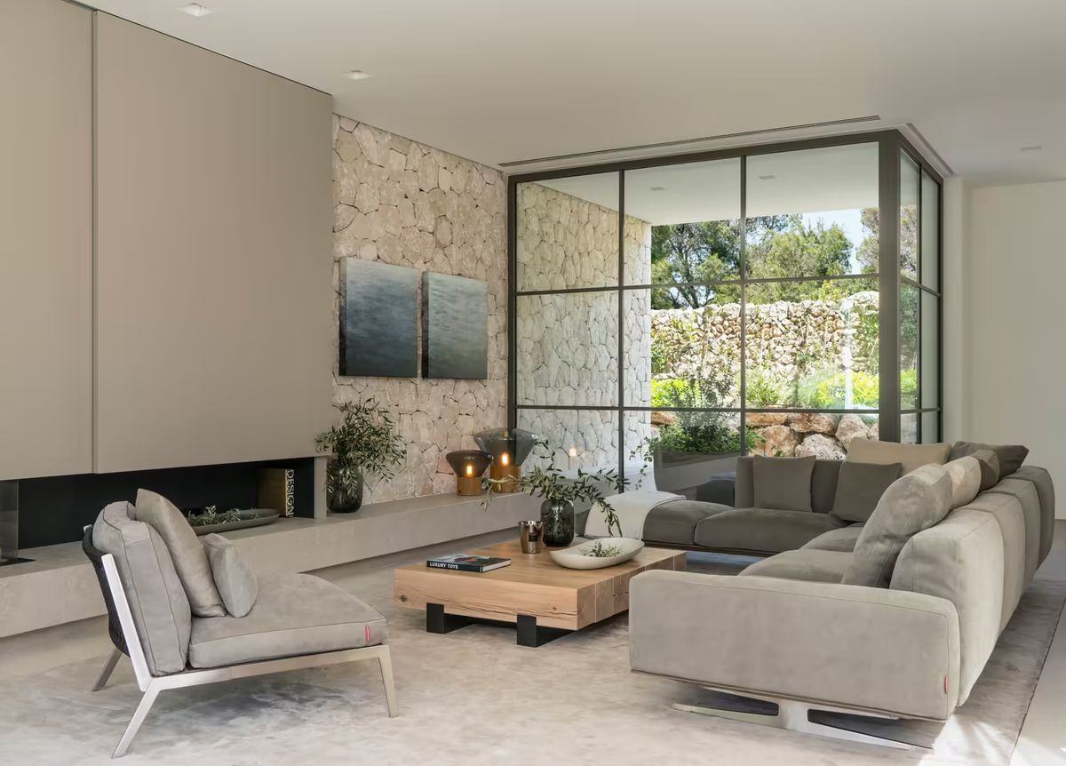 A living room with stone walls, large windows, Brokis Muffins lamps, art, and plants in a serene, luxurious setting.
