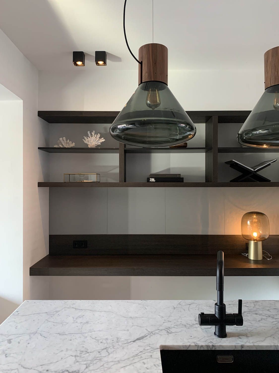 Modern kitchen with marble worktop, matte black tap, dark wood shelves, Brokis Muffins Wood 03B pendants above.