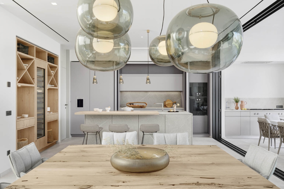 A kitchen-dining space features Brokis Big One Large pendant cluster, wooden table, chic seating, and sleek shelving.