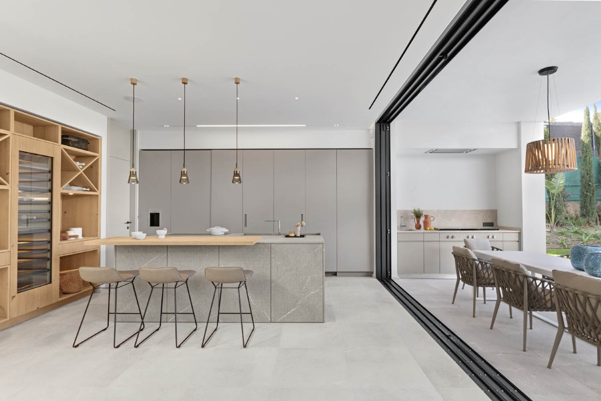 Kitchen with grey cabinetry, Brokis Shadows Narrow Pendants, a sleek island, and expansive glass doors to lush outdoors.