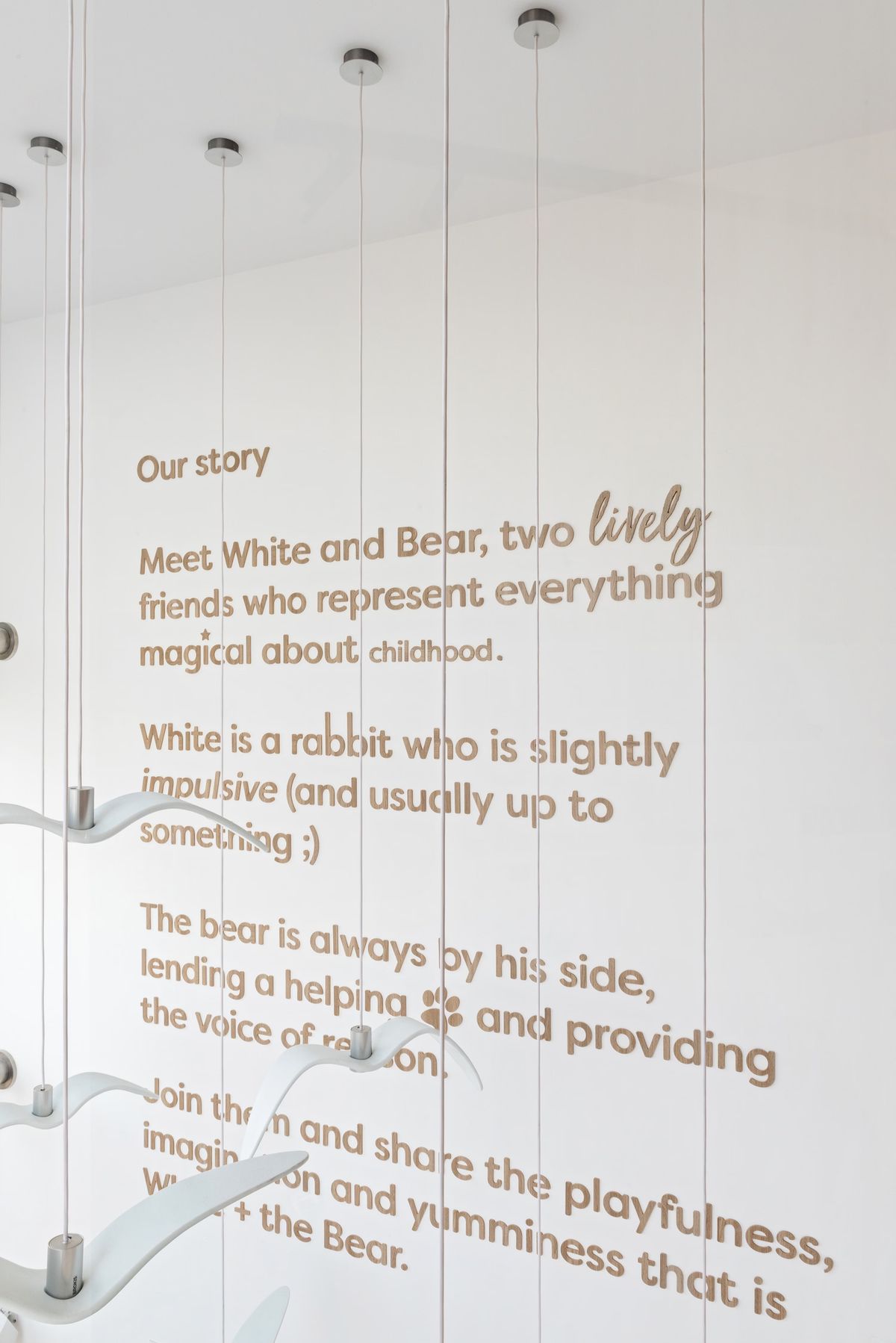 A wall with tan text introduces White and Bear café, set behind Brokis Night Birds pendants.