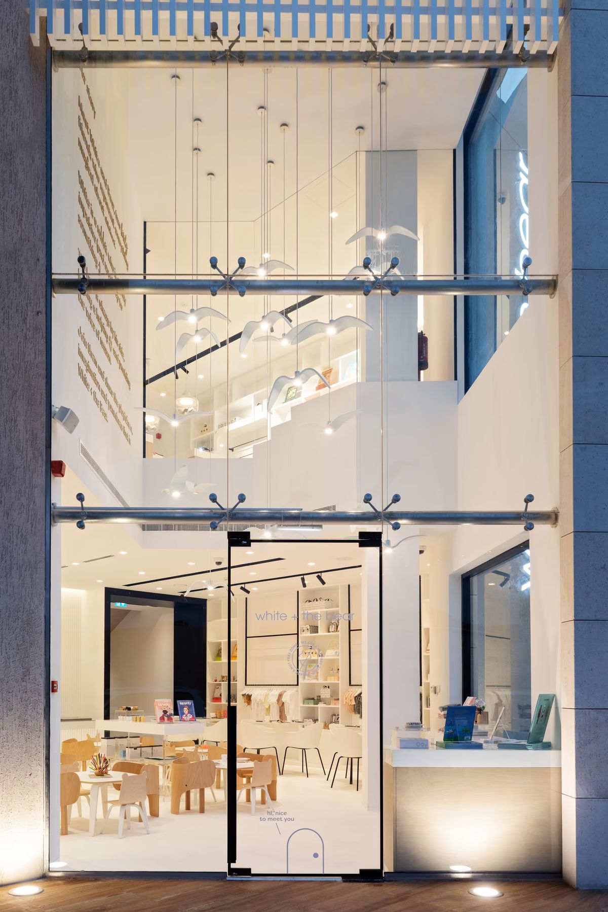 A shop with floor-to-ceiling glass windows, white walls, Brokis Night Birds pendants, creating a refined, welcoming space.
