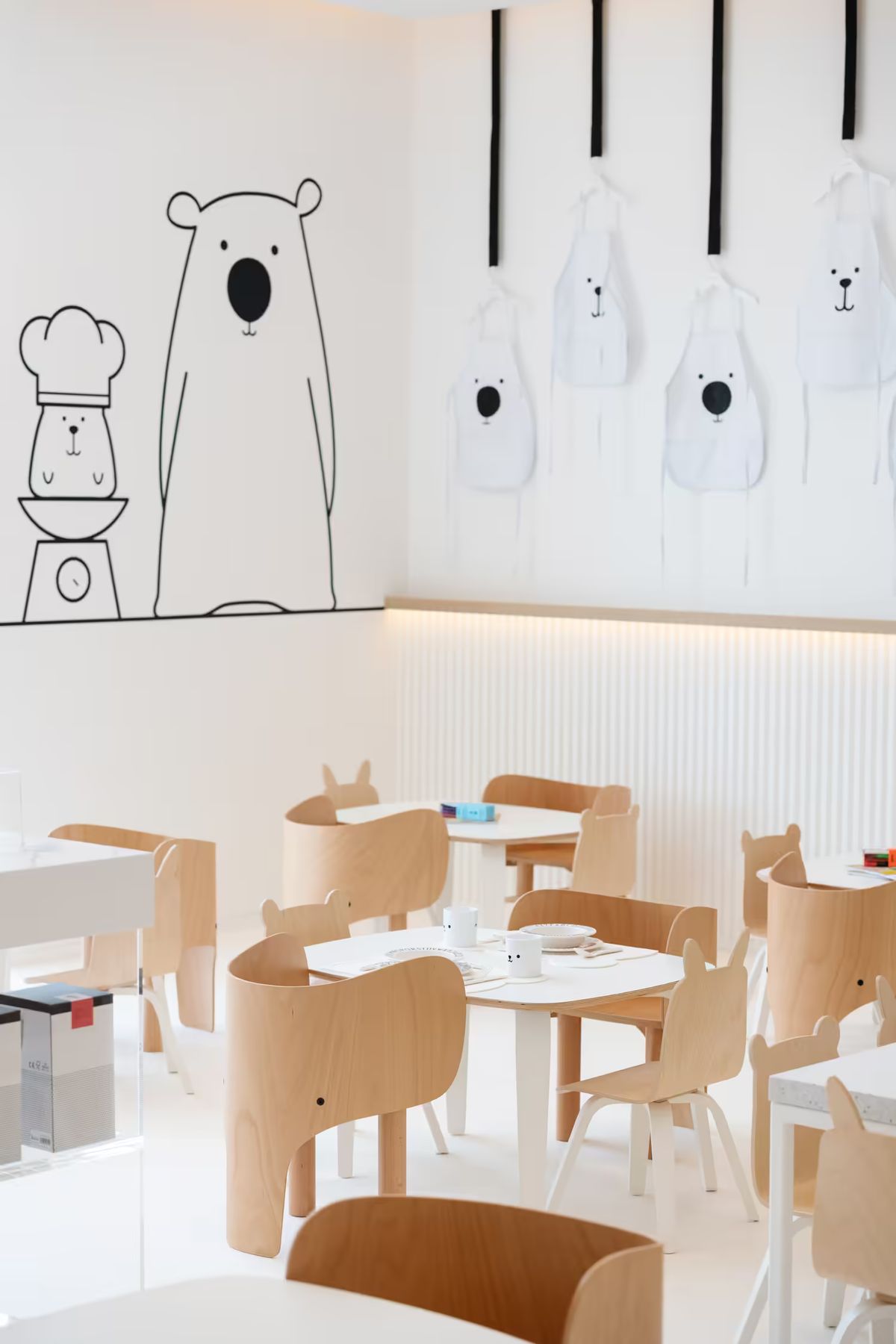 A bright, minimalist café with bear-shaped chairs, lighting, white tables, and playful bear-themed wall art.
