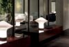 A modern interior with a glossy red sideboard, featuring an abstract mushroom-shaped white lamp, reflected in a glass wall. A leafy plant and a stylish living area with neutral tones are visible in the background.